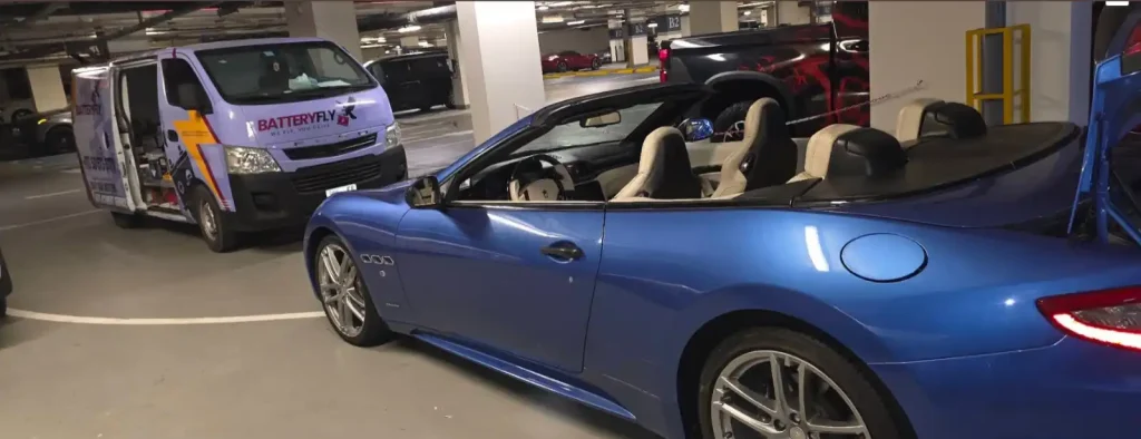 Batteryfly service van beside a blue Maserati convertible in underground parking.